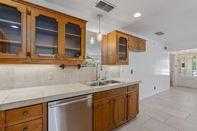 kitchen with stainless steel dishwasher, tasteful backsplash, sink, hanging light fixtures, and tile counters