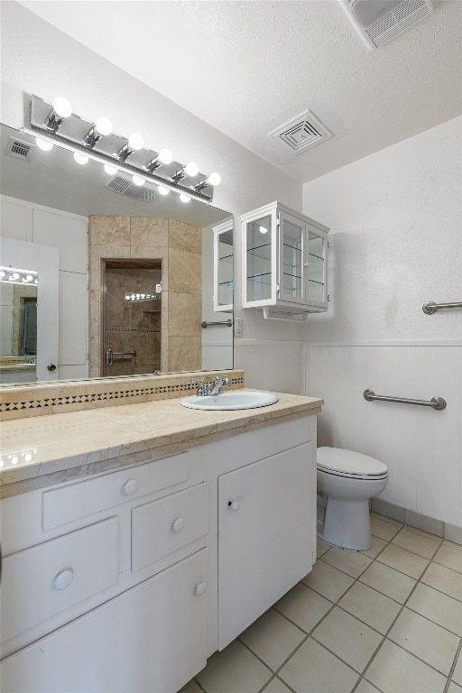 bathroom featuring a tile shower, vanity, tile patterned flooring, toilet, and a textured ceiling