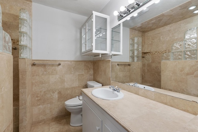 bathroom featuring tile walls, tiled shower, vanity, and toilet