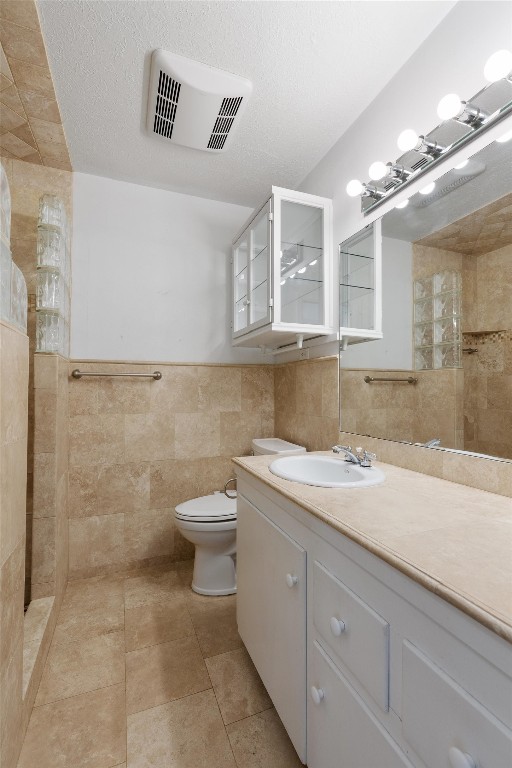 bathroom with vanity, tile walls, tiled shower, toilet, and a textured ceiling