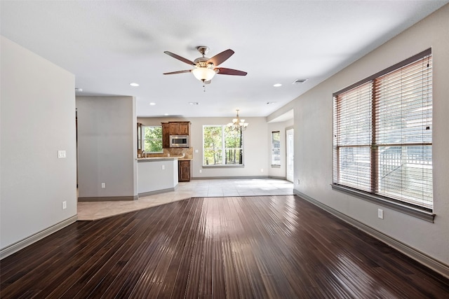 unfurnished living room with light hardwood / wood-style floors, sink, and ceiling fan with notable chandelier