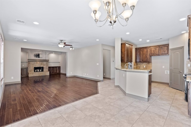 kitchen with a stone fireplace, light hardwood / wood-style flooring, kitchen peninsula, sink, and ceiling fan with notable chandelier