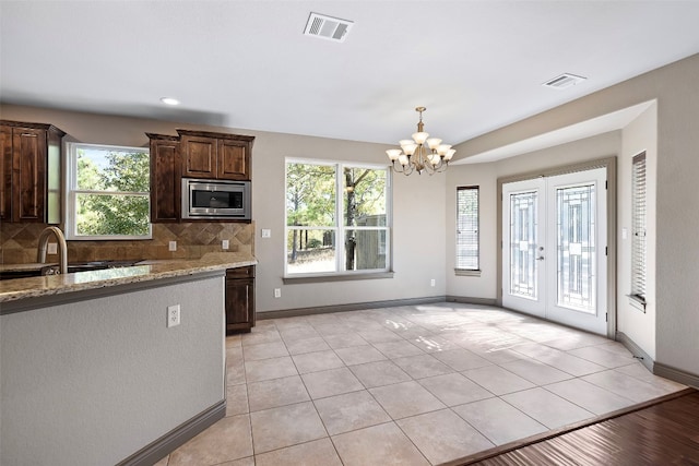 kitchen featuring a chandelier, light stone counters, stainless steel microwave, and backsplash