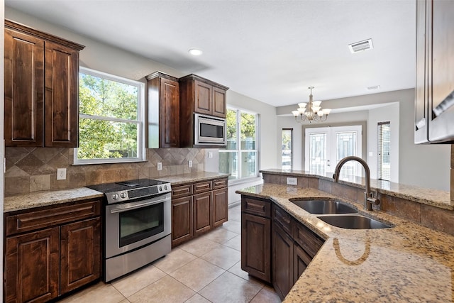 kitchen with tasteful backsplash, appliances with stainless steel finishes, sink, hanging light fixtures, and light stone counters