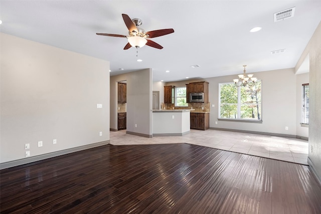 unfurnished living room featuring ceiling fan with notable chandelier and light wood-type flooring