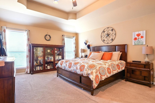 carpeted bedroom with a raised ceiling, multiple windows, and ceiling fan