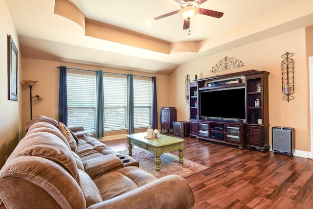 living room with ceiling fan, a tray ceiling, and dark hardwood / wood-style floors