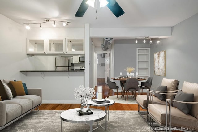living room with rail lighting, a ceiling fan, wood finished floors, and baseboards