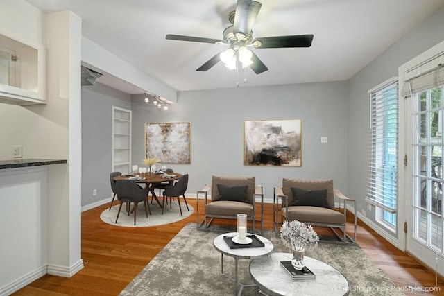 living area with wood finished floors, a ceiling fan, baseboards, and built in shelves