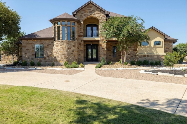 view of front facade with french doors, a shingled roof, and a balcony