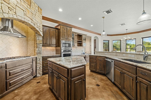 kitchen with appliances with stainless steel finishes, wall chimney range hood, sink, decorative light fixtures, and a kitchen island