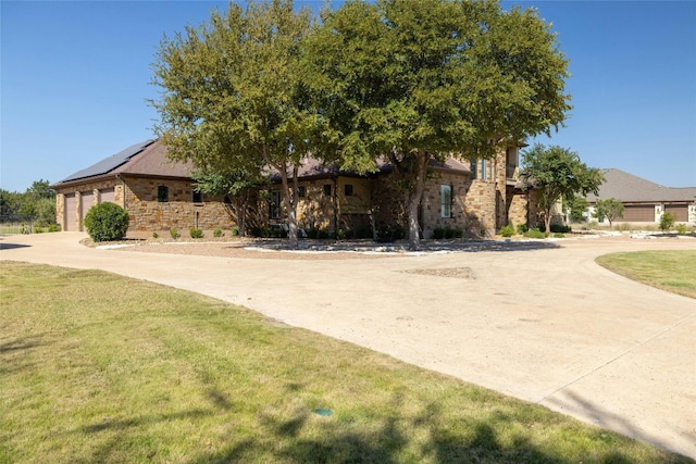 view of front of home featuring a front yard, stone siding, driveway, and solar panels