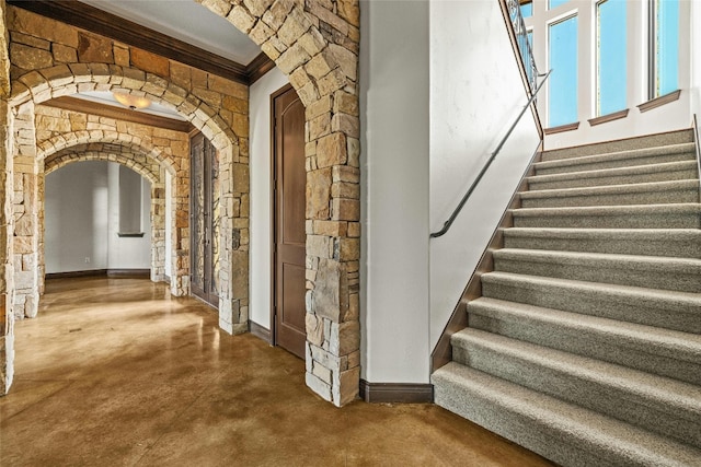 interior space featuring arched walkways, baseboards, finished concrete flooring, stairway, and crown molding