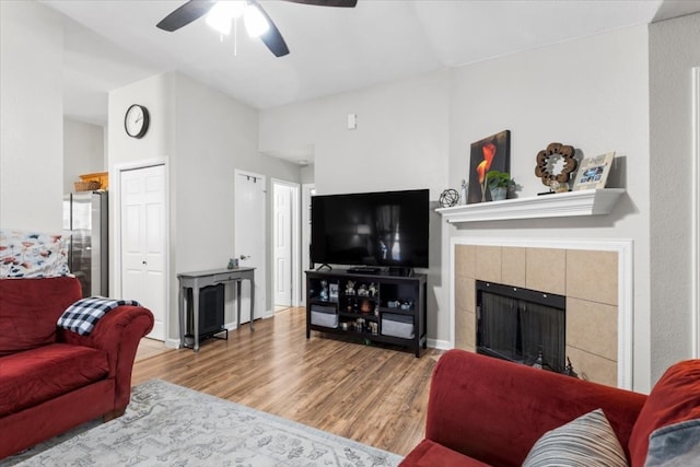 living room featuring ceiling fan, a tile fireplace, and hardwood / wood-style floors