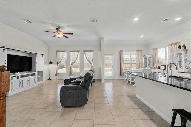 tiled living room with a healthy amount of sunlight, ceiling fan, a barn door, and sink