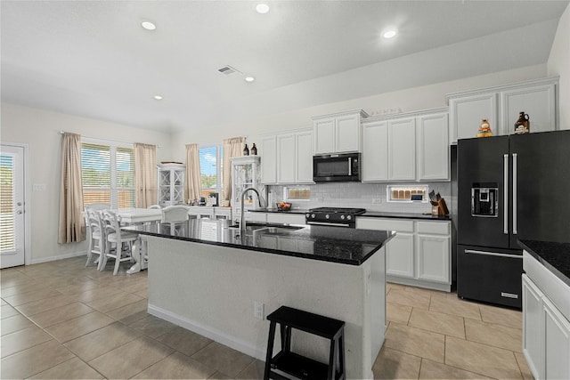 kitchen with sink, a center island with sink, backsplash, white cabinetry, and black appliances