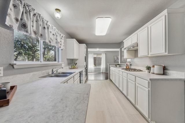 kitchen with stainless steel gas cooktop, light hardwood / wood-style floors, sink, and white cabinets