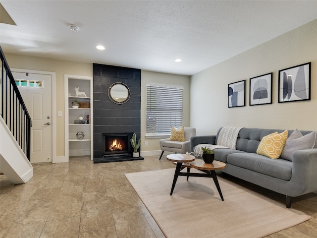 living room with built in shelves, a textured ceiling, and a tiled fireplace