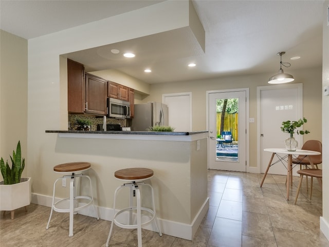 kitchen featuring stainless steel appliances, kitchen peninsula, a breakfast bar area, decorative light fixtures, and backsplash