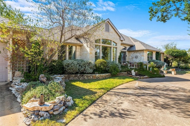 view of front of property featuring stone siding, concrete driveway, and a front yard