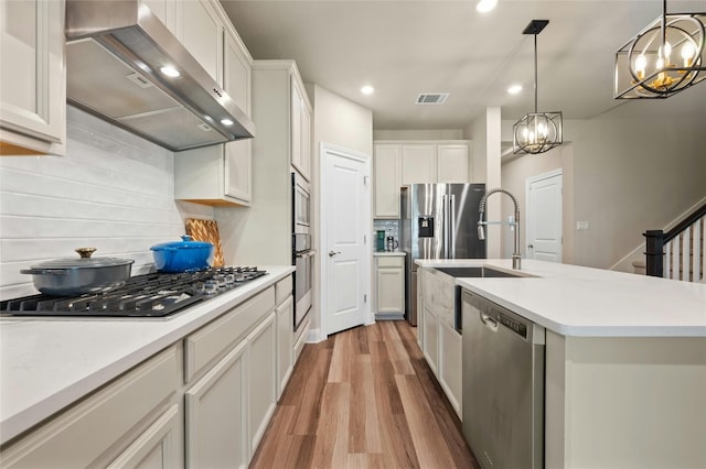 319 Victoria Peak Loop, Dripping Springs, TX 78620 - kitchen featuring wall chimney range hood, appliances with stainless steel finishes, light wood finished floors, a chandelier, and decorative backsplash