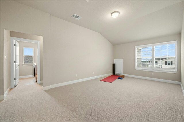 interior space featuring light carpet, visible vents, vaulted ceiling, and a wealth of natural light