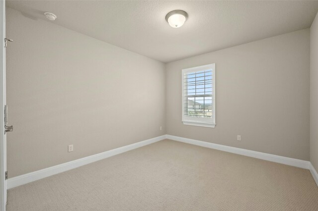 spare room featuring light carpet, a textured ceiling, and baseboards