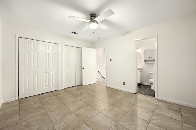 unfurnished bedroom with two closets, ceiling fan, light tile patterned floors, and ensuite bath