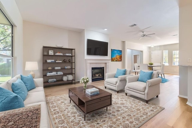 living room featuring ceiling fan, light hardwood / wood-style floors, and a tiled fireplace