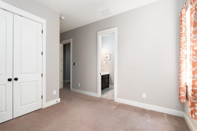 unfurnished bedroom with ensuite bath, light colored carpet, a closet, and baseboards