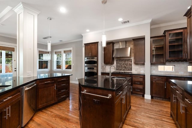 kitchen with a center island with sink, visible vents, a sink, stainless steel appliances, and wall chimney range hood