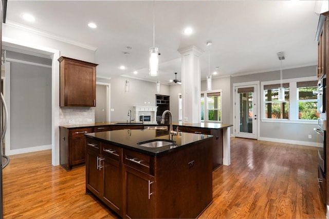 kitchen featuring an island with sink, a sink, backsplash, wood finished floors, and open floor plan