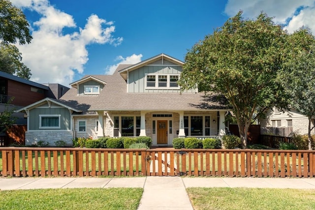 craftsman-style home with a fenced front yard, board and batten siding, stone siding, and a shingled roof