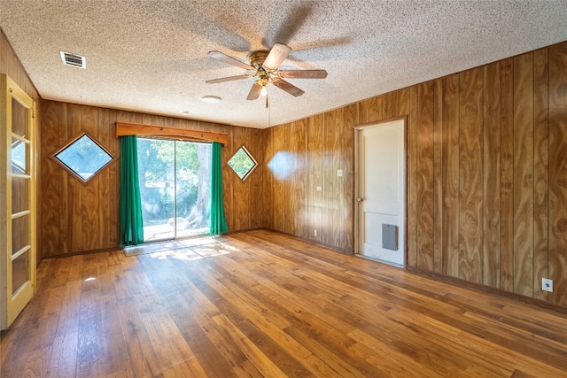 unfurnished room featuring hardwood / wood-style floors, wooden walls, and a textured ceiling