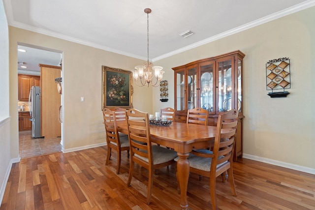 dining space featuring wood-type flooring, ornamental molding, and a notable chandelier