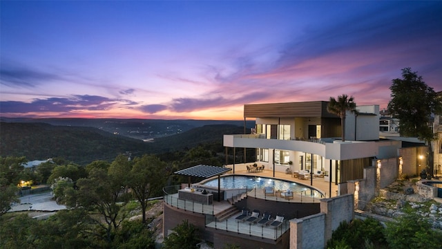 back house at dusk featuring an outdoor living space, a mountain view, a balcony, and a patio area