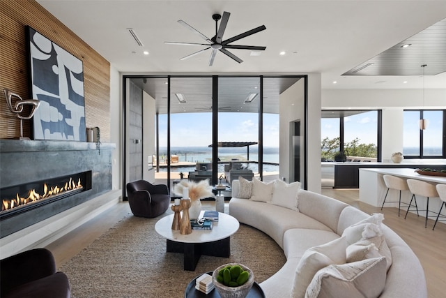 living room featuring a wall of windows, a water view, ceiling fan, and light hardwood / wood-style floors