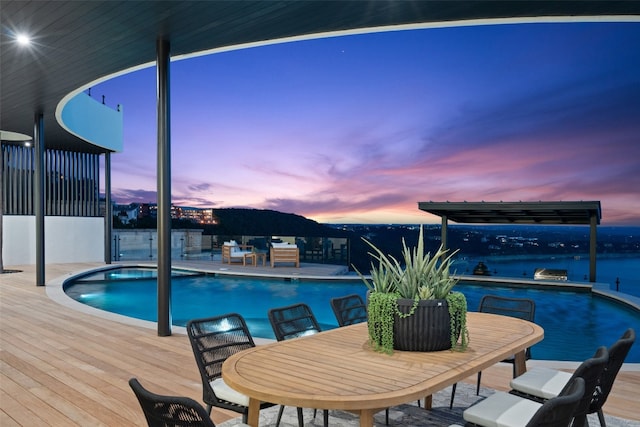 pool at dusk featuring a water view and a patio area