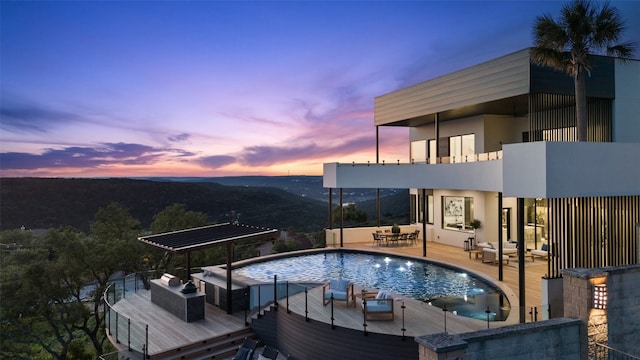 pool at dusk with outdoor lounge area and a wooden deck