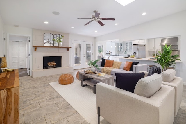 living room featuring ceiling fan, a tiled fireplace, and french doors