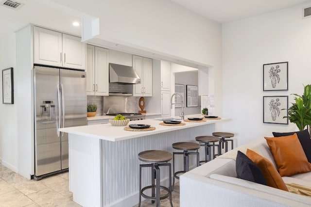 kitchen with a kitchen breakfast bar, range hood, kitchen peninsula, white cabinets, and appliances with stainless steel finishes