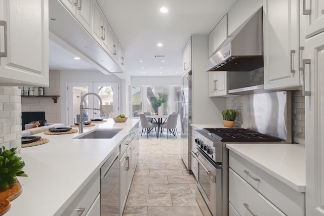 kitchen with sink, backsplash, wall chimney range hood, white cabinetry, and appliances with stainless steel finishes