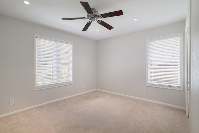 spare room with ceiling fan, a wealth of natural light, and light carpet