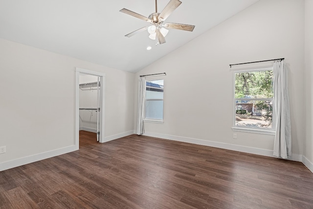 unfurnished bedroom featuring a closet, a walk in closet, vaulted ceiling, dark wood-type flooring, and ceiling fan