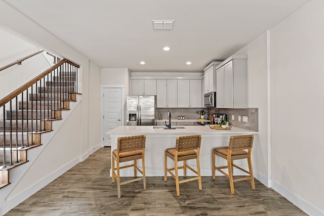 kitchen featuring light hardwood / wood-style floors, kitchen peninsula, sink, a breakfast bar, and appliances with stainless steel finishes