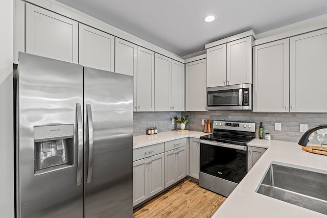 kitchen featuring light hardwood / wood-style floors, stainless steel appliances, sink, tasteful backsplash, and gray cabinetry