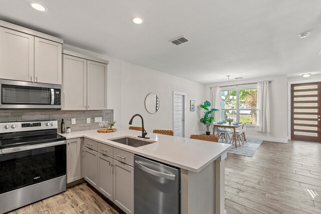 kitchen with light wood-type flooring, kitchen peninsula, sink, and stainless steel appliances