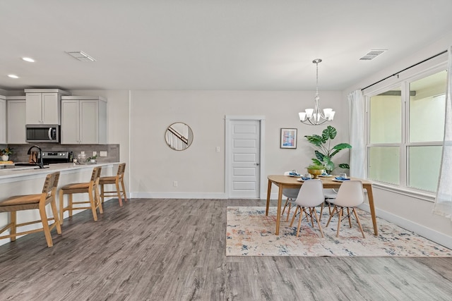 dining area with light hardwood / wood-style floors, sink, and a notable chandelier