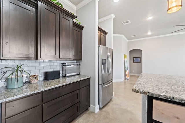 kitchen featuring light stone countertops, stainless steel refrigerator with ice dispenser, ornamental molding, dark brown cabinets, and backsplash