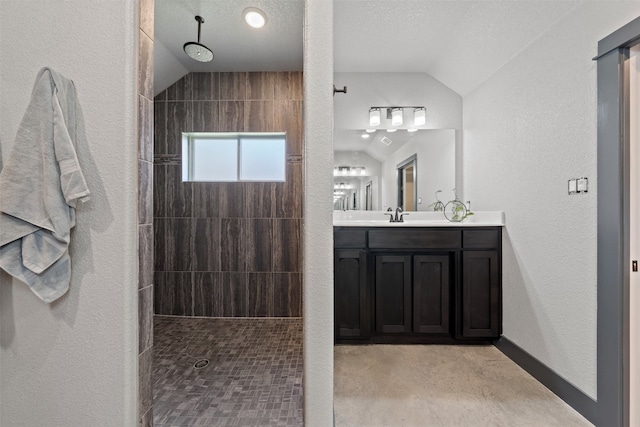 bathroom featuring vanity, vaulted ceiling, a textured ceiling, and tiled shower